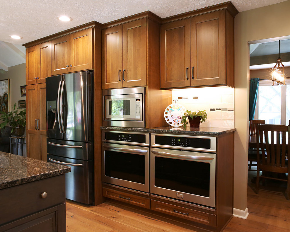 Photo of a large classic u-shaped kitchen pantry in Omaha with a double-bowl sink, recessed-panel cabinets, dark wood cabinets, granite worktops, white splashback, metro tiled splashback, stainless steel appliances, medium hardwood flooring, an island, brown floors, grey worktops and a vaulted ceiling.