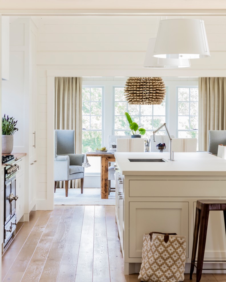 Design ideas for a beach style open plan kitchen in Boston with an undermount sink, shaker cabinets, white cabinets, light hardwood floors and with island.