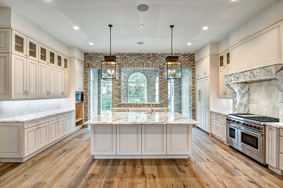 This is an example of a traditional kitchen in Houston with marble benchtops, light hardwood floors and with island.