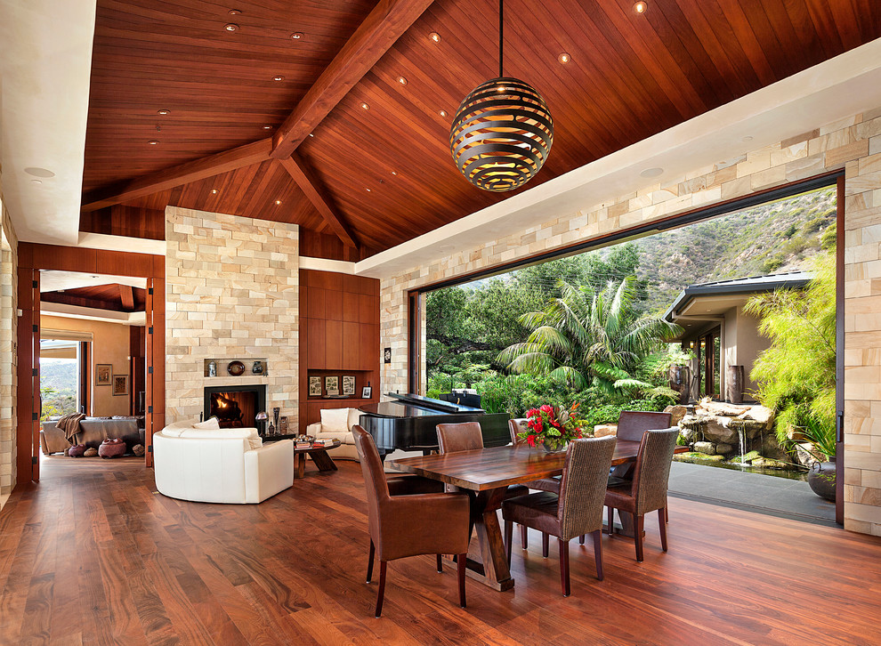 Design ideas for an expansive tropical dining room in Santa Barbara with beige walls, dark hardwood floors, a stone fireplace surround and a standard fireplace.