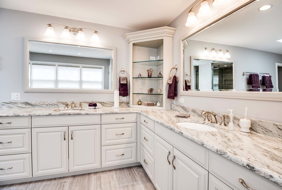 Inspiration for a large transitional master brown tile, beige tile and porcelain tile porcelain tile and beige floor freestanding bathtub remodel in Chicago with raised-panel cabinets, white cabinets, beige walls, an undermount sink, granite countertops, a hinged shower door and beige countertops
