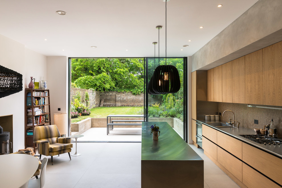 This is an example of a contemporary galley open plan kitchen in London with a double-bowl sink, flat-panel cabinets, medium wood cabinets, stainless steel benchtops, brown splashback, mosaic tile splashback, black appliances, with island and white floor.