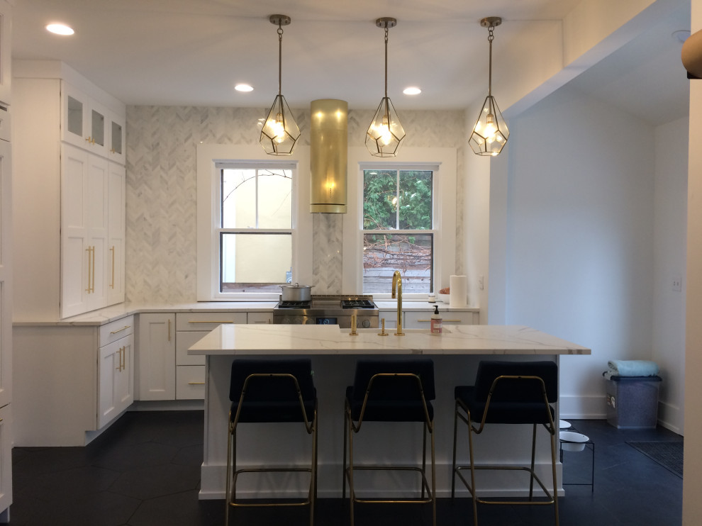Photo of a mid-sized transitional l-shaped eat-in kitchen in New York with a farmhouse sink, shaker cabinets, white cabinets, quartzite benchtops, grey splashback, stone tile splashback, ceramic floors, with island, black floor and white benchtop.