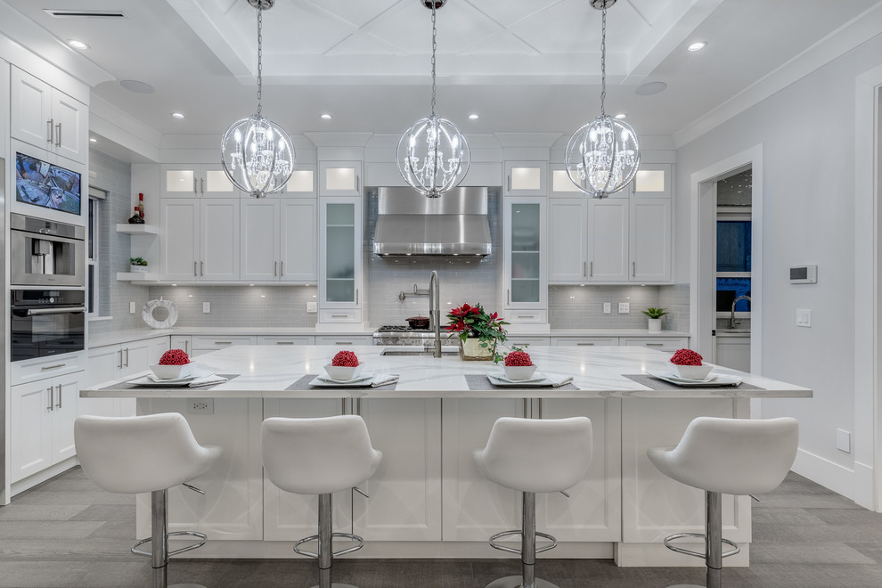 This is an example of a large contemporary l-shaped open plan kitchen in Vancouver with a double-bowl sink, shaker cabinets, white cabinets, marble benchtops, grey splashback, subway tile splashback, stainless steel appliances, light hardwood floors, with island and brown floor.