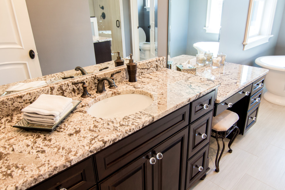 Inspiration for a large transitional master beige tile and ceramic tile ceramic tile freestanding bathtub remodel in Providence with an undermount sink, raised-panel cabinets, dark wood cabinets, granite countertops, a two-piece toilet and gray walls