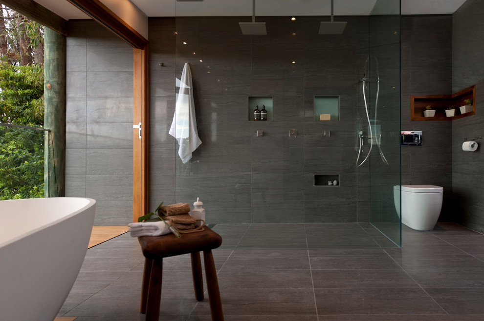 Photo of a contemporary bathroom in Sydney with a freestanding tub, a one-piece toilet, gray tile, grey walls and ceramic floors.