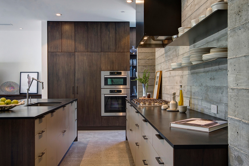 This is an example of a large country l-shaped kitchen pantry in San Francisco with an undermount sink, flat-panel cabinets, dark wood cabinets, solid surface benchtops, grey splashback, panelled appliances, concrete floors and with island.