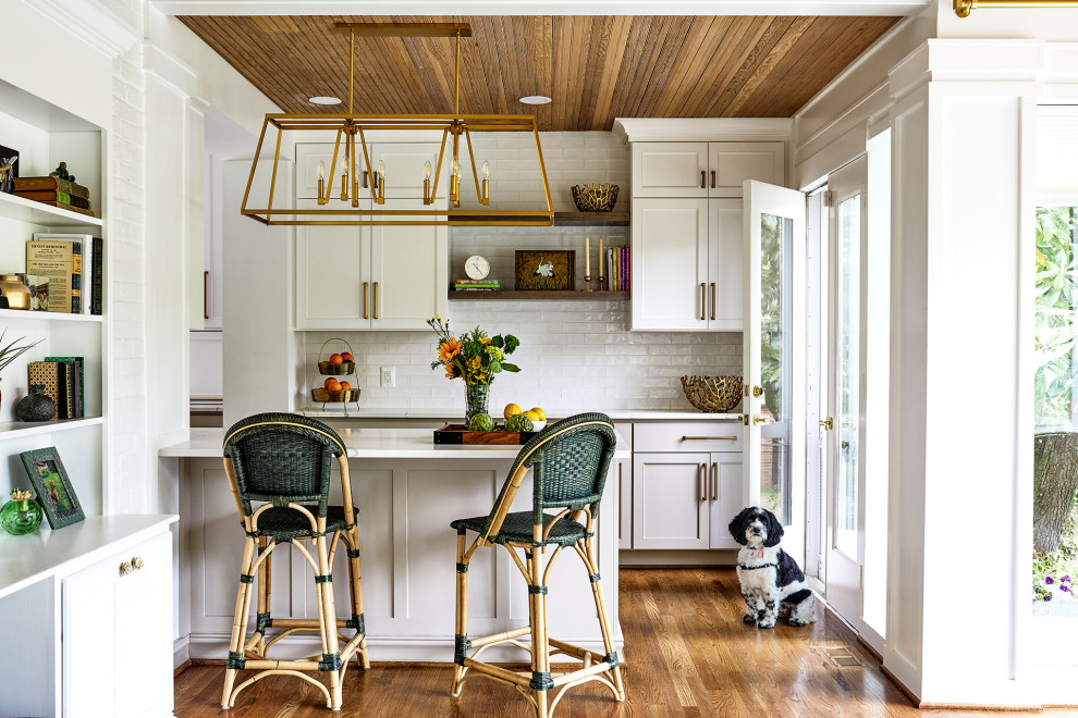 Design ideas for a traditional galley kitchen in DC Metro with shaker cabinets, white cabinets, white splashback, medium hardwood flooring, an island, brown floors, white worktops and a wood ceiling.