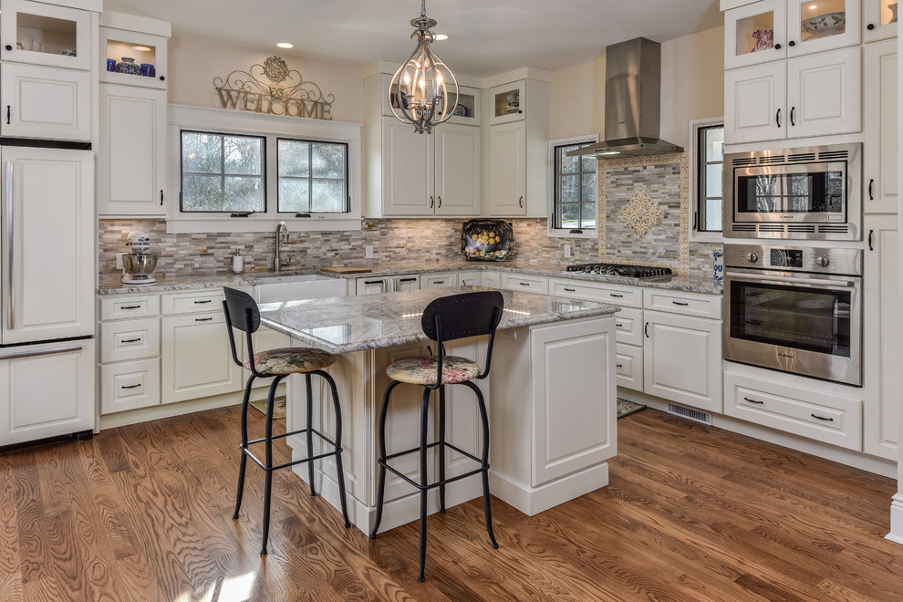 Example of a large transitional l-shaped medium tone wood floor kitchen design with a farmhouse sink, raised-panel cabinets, white cabinets, granite countertops, multicolored backsplash, matchstick tile backsplash, stainless steel appliances and an island