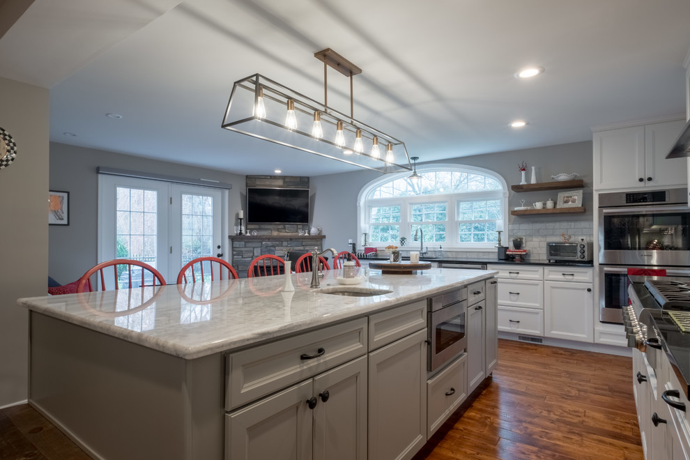 Inspiration for a large country kitchen in Philadelphia with an undermount sink, shaker cabinets, white cabinets, granite benchtops, white splashback, marble splashback, stainless steel appliances, medium hardwood floors, with island, brown floor and black benchtop.