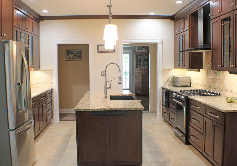 Photo of a large traditional galley eat-in kitchen in Nashville with a farmhouse sink, shaker cabinets, dark wood cabinets, granite benchtops, beige splashback, travertine splashback, stainless steel appliances, porcelain floors, with island, beige floor and beige benchtop.