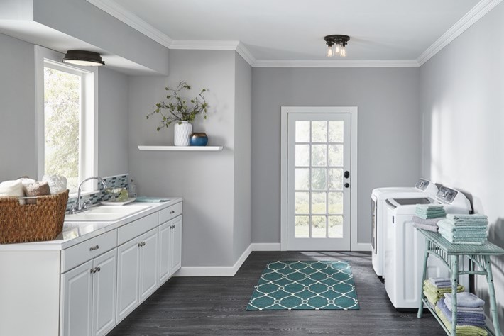 This is an example of a transitional galley dedicated laundry room in Other with a double-bowl sink, recessed-panel cabinets, white cabinets, grey walls, laminate floors, a side-by-side washer and dryer and grey floor.