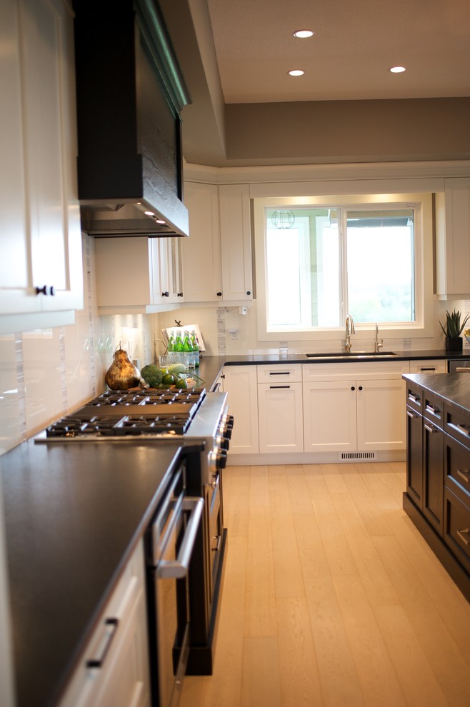 Large transitional u-shaped light wood floor eat-in kitchen photo in Edmonton with a farmhouse sink, shaker cabinets, white cabinets, granite countertops, white backsplash, stone tile backsplash, stainless steel appliances and an island