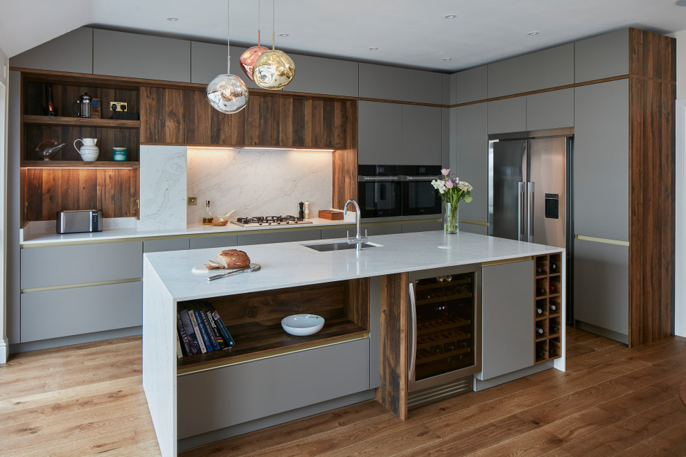 Design ideas for a large contemporary l-shaped open plan kitchen in London with a drop-in sink, flat-panel cabinets, grey cabinets, quartzite benchtops, grey splashback, engineered quartz splashback, stainless steel appliances, medium hardwood floors, with island and grey benchtop.