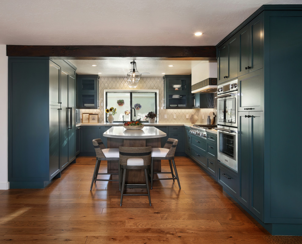 Photo of a large mediterranean u-shaped enclosed kitchen in Orange County with a submerged sink, shaker cabinets, green cabinets, engineered stone countertops, beige splashback, ceramic splashback, integrated appliances, medium hardwood flooring, an island, brown floors and beige worktops.