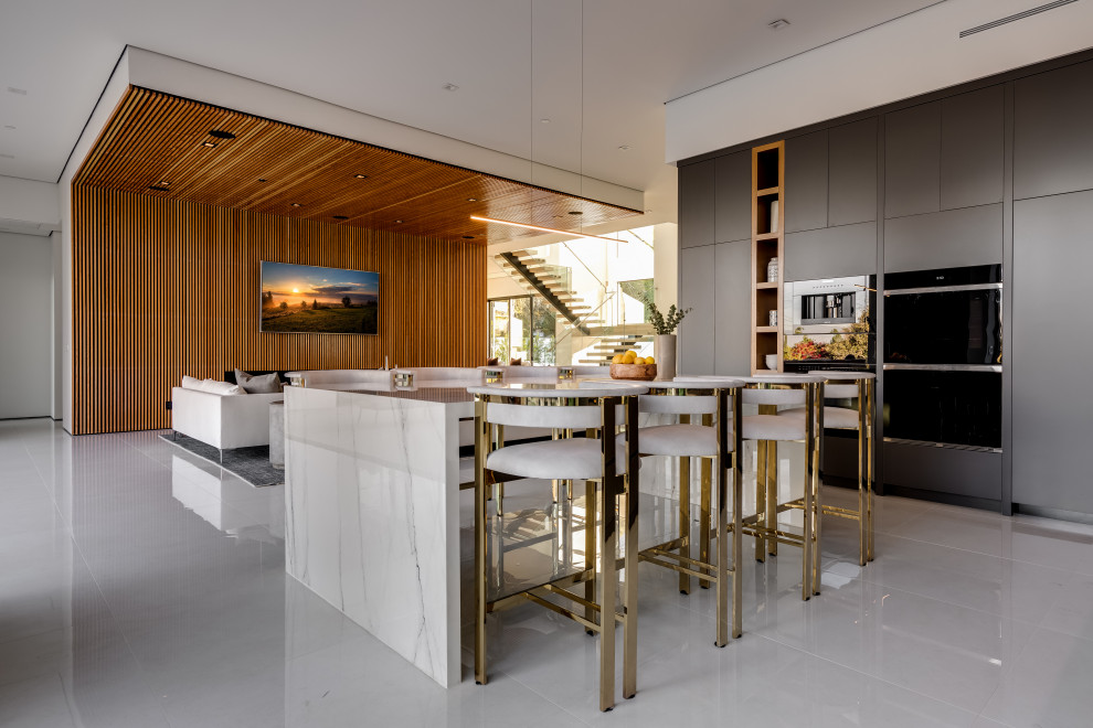 Photo of an expansive contemporary galley eat-in kitchen in Los Angeles with an undermount sink, flat-panel cabinets, grey cabinets, solid surface benchtops, white splashback, porcelain splashback, black appliances, porcelain floors, multiple islands, white floor and white benchtop.