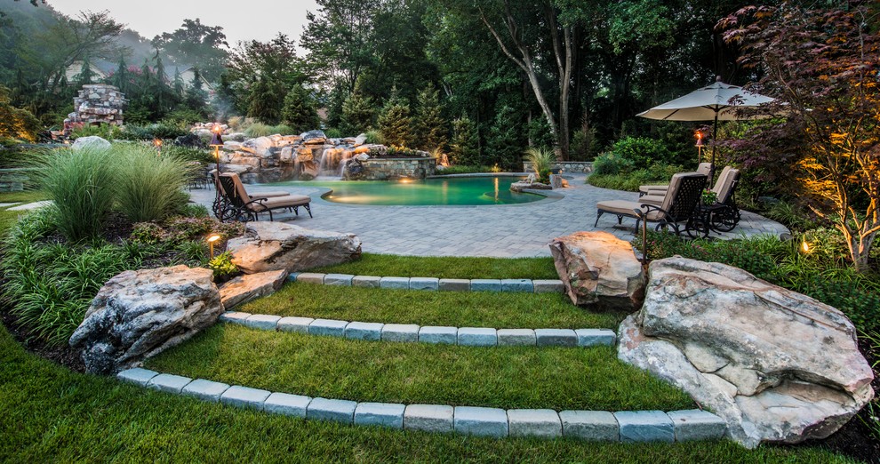 This is an example of a mid-sized country backyard custom-shaped lap pool in DC Metro with a water feature and concrete pavers.