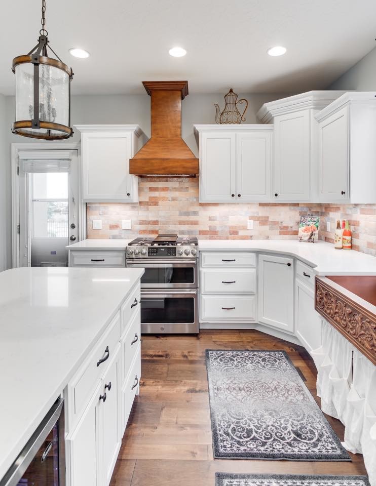 Photo of a mid-sized country u-shaped eat-in kitchen in Salt Lake City with a farmhouse sink, recessed-panel cabinets, white cabinets, quartzite benchtops, brown splashback, ceramic splashback, stainless steel appliances, medium hardwood floors, with island, brown floor and white benchtop.