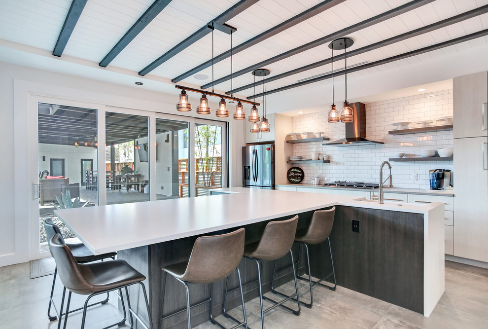 This is an example of a mid-sized industrial single-wall open plan kitchen in Tampa with a farmhouse sink, shaker cabinets, white cabinets, white splashback, subway tile splashback, stainless steel appliances, cement tiles, with island, grey floor and white benchtop.