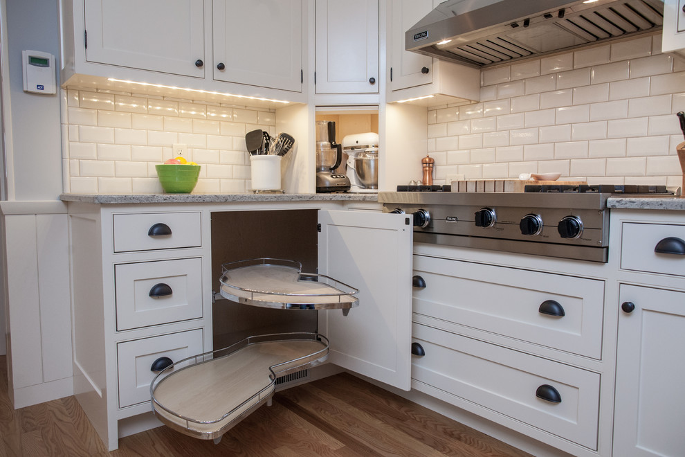 This is an example of a mid-sized industrial l-shaped open plan kitchen in Grand Rapids with an undermount sink, recessed-panel cabinets, white cabinets, quartz benchtops, white splashback, ceramic splashback, stainless steel appliances, light hardwood floors and no island.