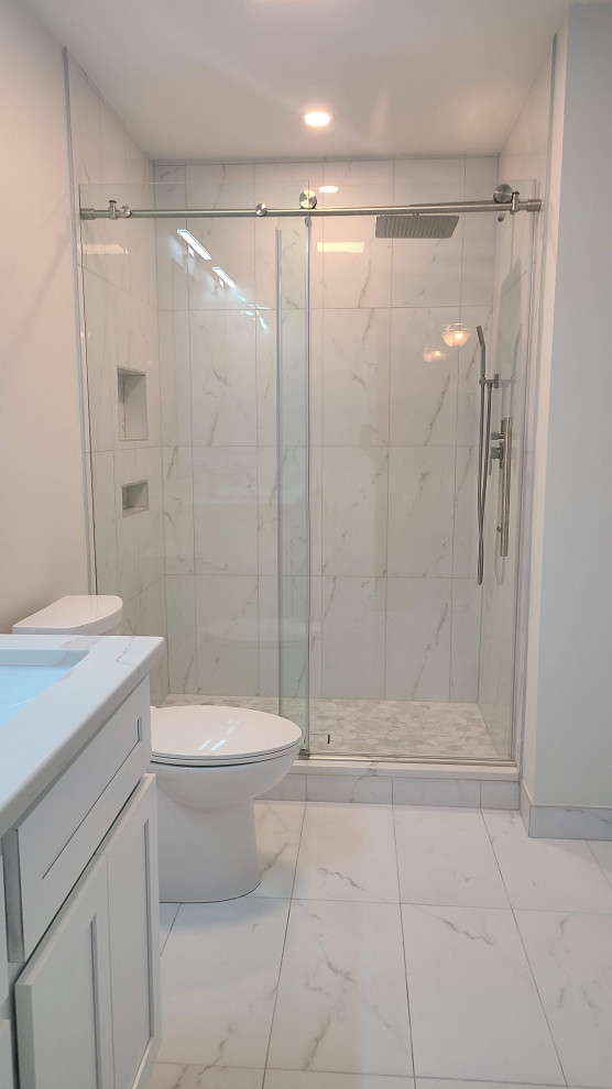 Réalisation d'une salle de bain grise et blanche minimaliste de taille moyenne avec un placard à porte shaker, des portes de placard blanches, WC à poser, un carrelage blanc, des dalles de pierre, un mur blanc, un sol en carrelage de porcelaine, un lavabo encastré, un plan de toilette en granite, un sol blanc, une cabine de douche à porte coulissante, un plan de toilette blanc, meuble simple vasque, meuble-lavabo encastré et un plafond voûté.