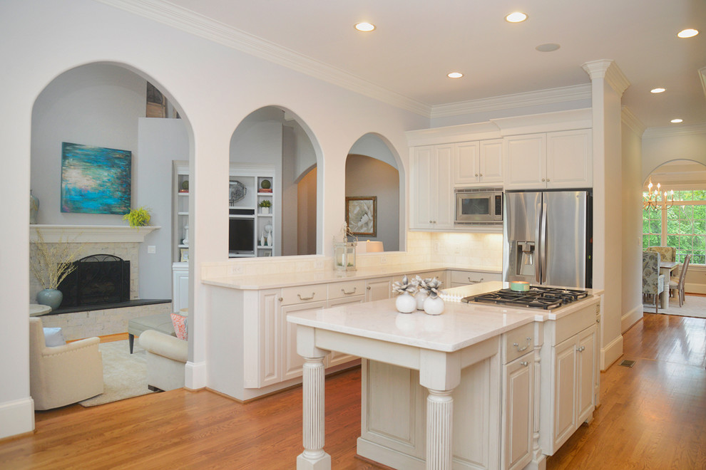 Example of a transitional light wood floor kitchen design with white cabinets, beige backsplash, stainless steel appliances and an island