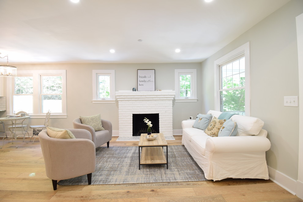 Photo of a mid-sized arts and crafts open concept living room in Baltimore with a library, grey walls, light hardwood floors, a standard fireplace, a brick fireplace surround, no tv and multi-coloured floor.