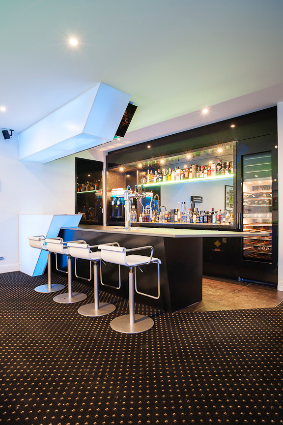This is an example of a large contemporary galley seated home bar in Melbourne with an undermount sink, flat-panel cabinets, black cabinets, solid surface benchtops, porcelain floors and mirror splashback.