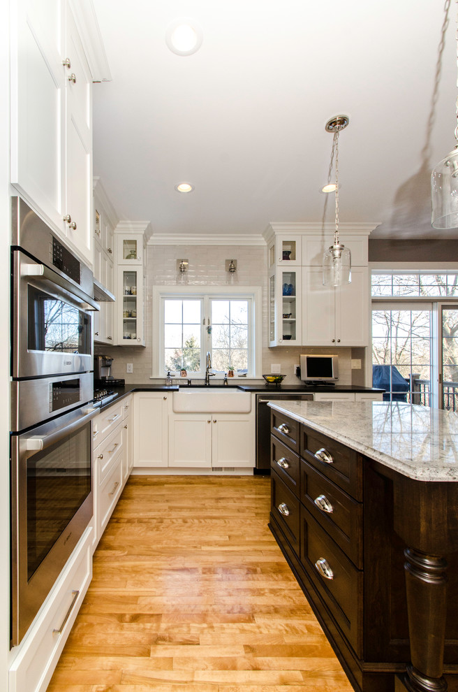 Inspiration for a mid-sized traditional l-shaped eat-in kitchen in Milwaukee with a farmhouse sink, recessed-panel cabinets, white cabinets, granite benchtops, white splashback, subway tile splashback, stainless steel appliances, medium hardwood floors and with island.