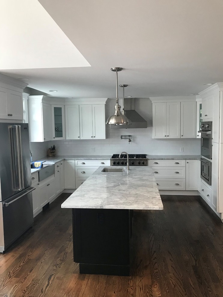 Mid-sized transitional u-shaped dark wood floor and brown floor eat-in kitchen photo in New York with a farmhouse sink, recessed-panel cabinets, white cabinets, wood countertops, white backsplash, limestone backsplash, stainless steel appliances, an island and white countertops