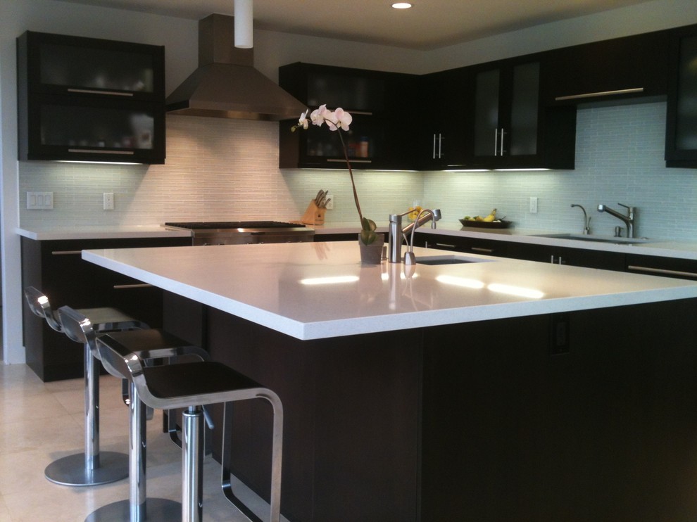 Photo of a mid-sized modern l-shaped eat-in kitchen in Los Angeles with flat-panel cabinets, quartz benchtops, white splashback, stainless steel appliances, travertine floors, with island, black cabinets, matchstick tile splashback and a double-bowl sink.