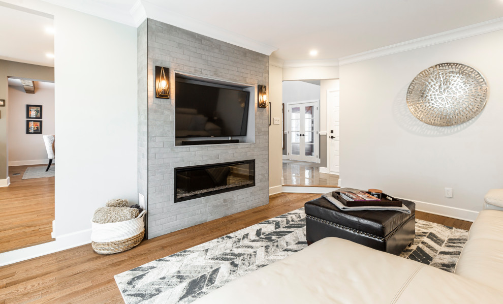 Пример оригинального дизайна: открытая гостиная комната в стиле кантри с серыми стенами, паркетным полом среднего тона, горизонтальным камином, фасадом камина из кирпича, скрытым телевизором и коричневым полом