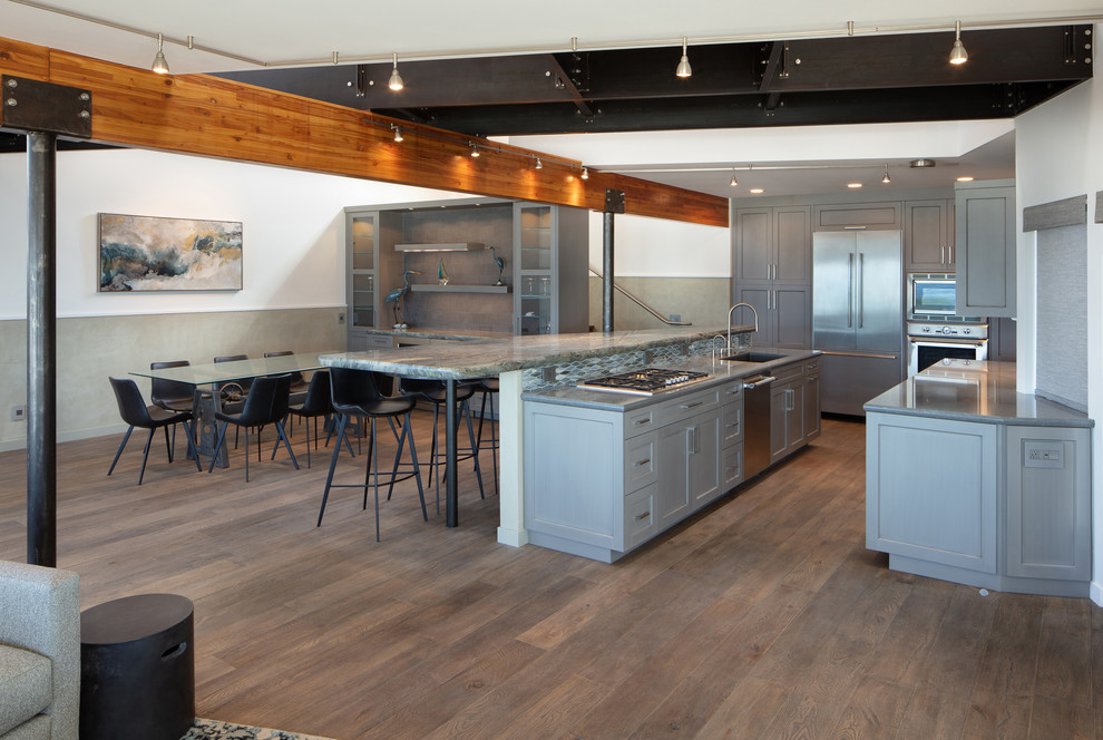 Photo of a mid-sized contemporary l-shaped open plan kitchen in San Luis Obispo with an undermount sink, shaker cabinets, grey cabinets, blue splashback, glass tile splashback, stainless steel appliances, dark hardwood floors, with island, brown floor and grey benchtop.