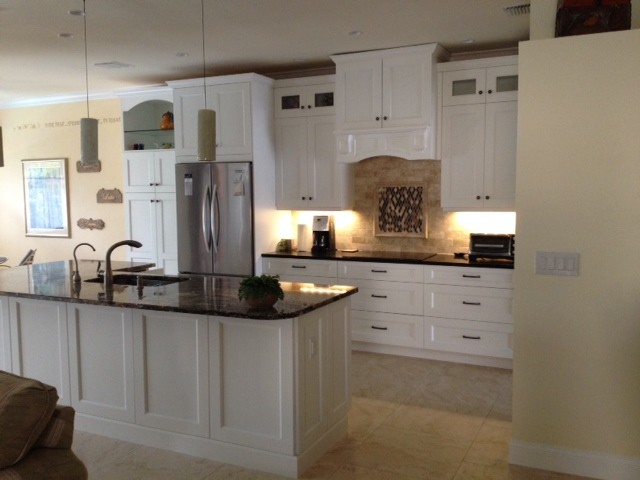 Example of a mid-sized transitional travertine floor open concept kitchen design with an undermount sink, shaker cabinets, white cabinets, granite countertops, beige backsplash, stone tile backsplash, stainless steel appliances and an island