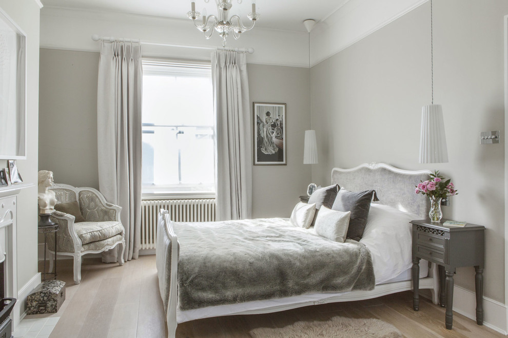 This is an example of a traditional master bedroom in London with grey walls and light hardwood floors.
