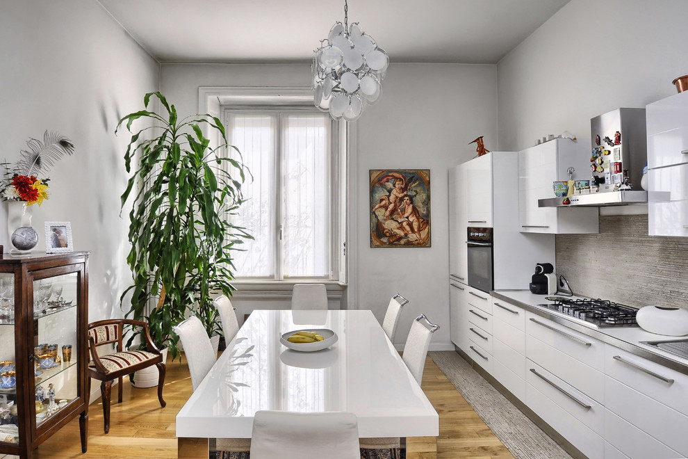 Photo of a contemporary eat-in kitchen in Milan with flat-panel cabinets, white cabinets, grey splashback, light hardwood floors, white benchtop and mosaic tile splashback.