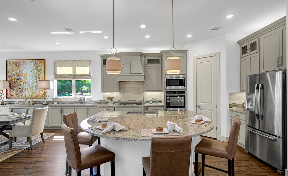 This is an example of a large contemporary l-shaped eat-in kitchen in Dallas with an undermount sink, raised-panel cabinets, beige cabinets, granite benchtops, beige splashback, ceramic splashback, stainless steel appliances, medium hardwood floors, with island and brown floor.
