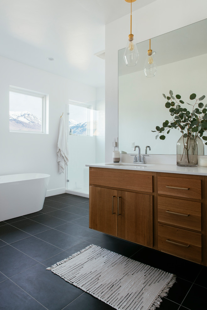 This is an example of a contemporary bathroom in Salt Lake City with flat-panel cabinets, medium wood cabinets, a freestanding tub, an alcove shower, white walls, an undermount sink and black floor.