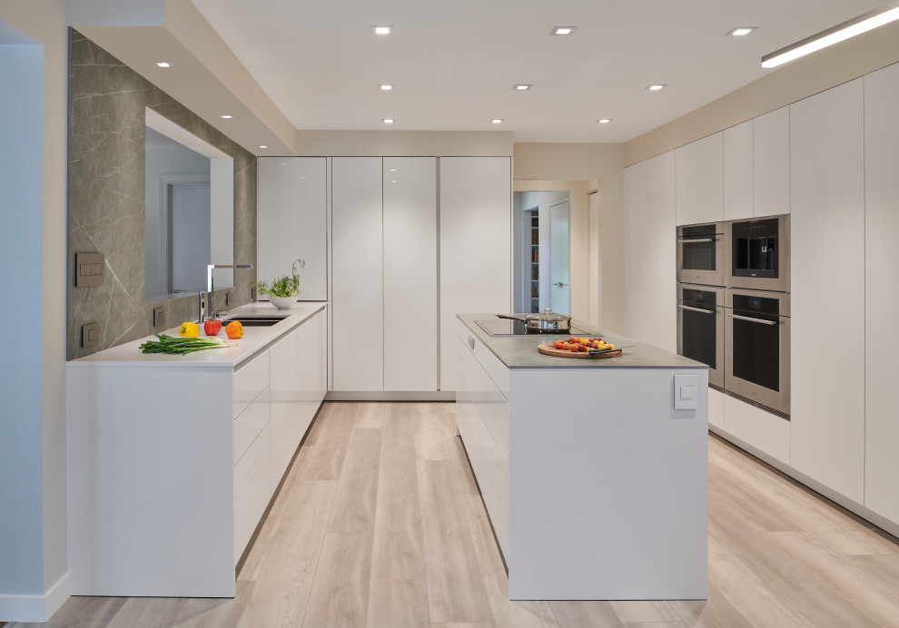 This is an example of a mid-sized contemporary u-shaped eat-in kitchen in DC Metro with an undermount sink, flat-panel cabinets, white cabinets, quartzite benchtops, grey splashback, engineered quartz splashback, stainless steel appliances, vinyl floors, with island, grey floor and grey benchtop.
