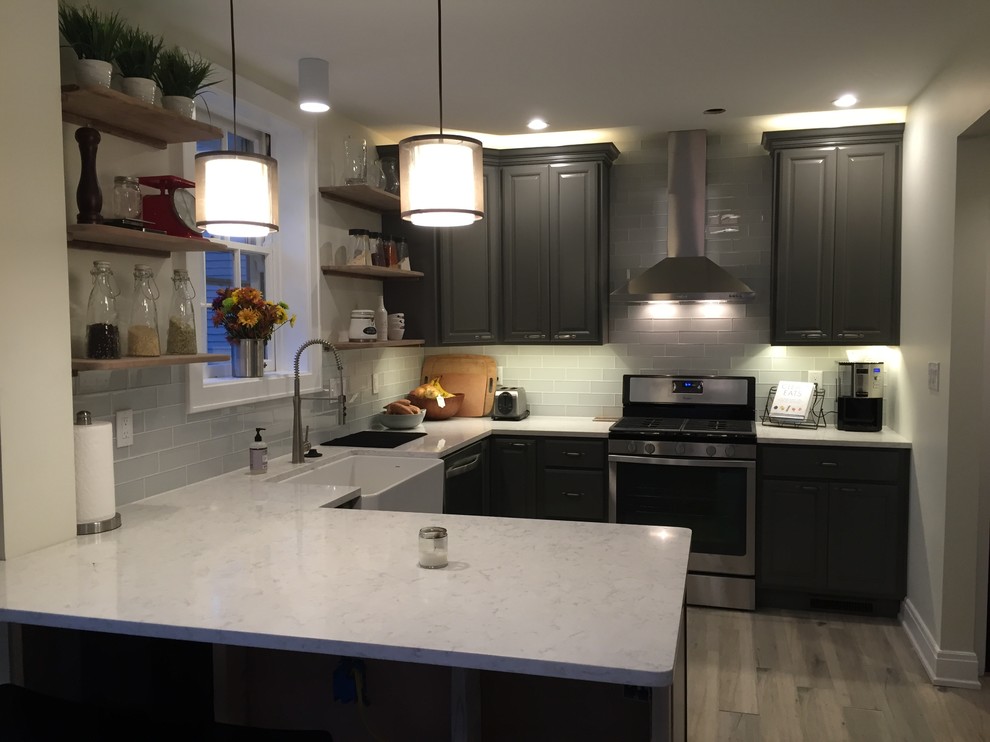 Eat-in kitchen - small transitional u-shaped light wood floor eat-in kitchen idea in Cincinnati with a farmhouse sink, raised-panel cabinets, gray cabinets, quartz countertops, gray backsplash, glass tile backsplash, stainless steel appliances and a peninsula