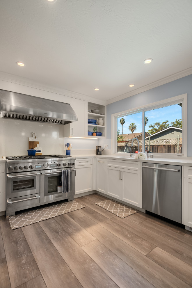 This is an example of a mid-sized contemporary l-shaped eat-in kitchen in San Francisco with an undermount sink, shaker cabinets, white cabinets, quartzite benchtops, white splashback, porcelain splashback, stainless steel appliances, vinyl floors, a peninsula, brown floor and white benchtop.