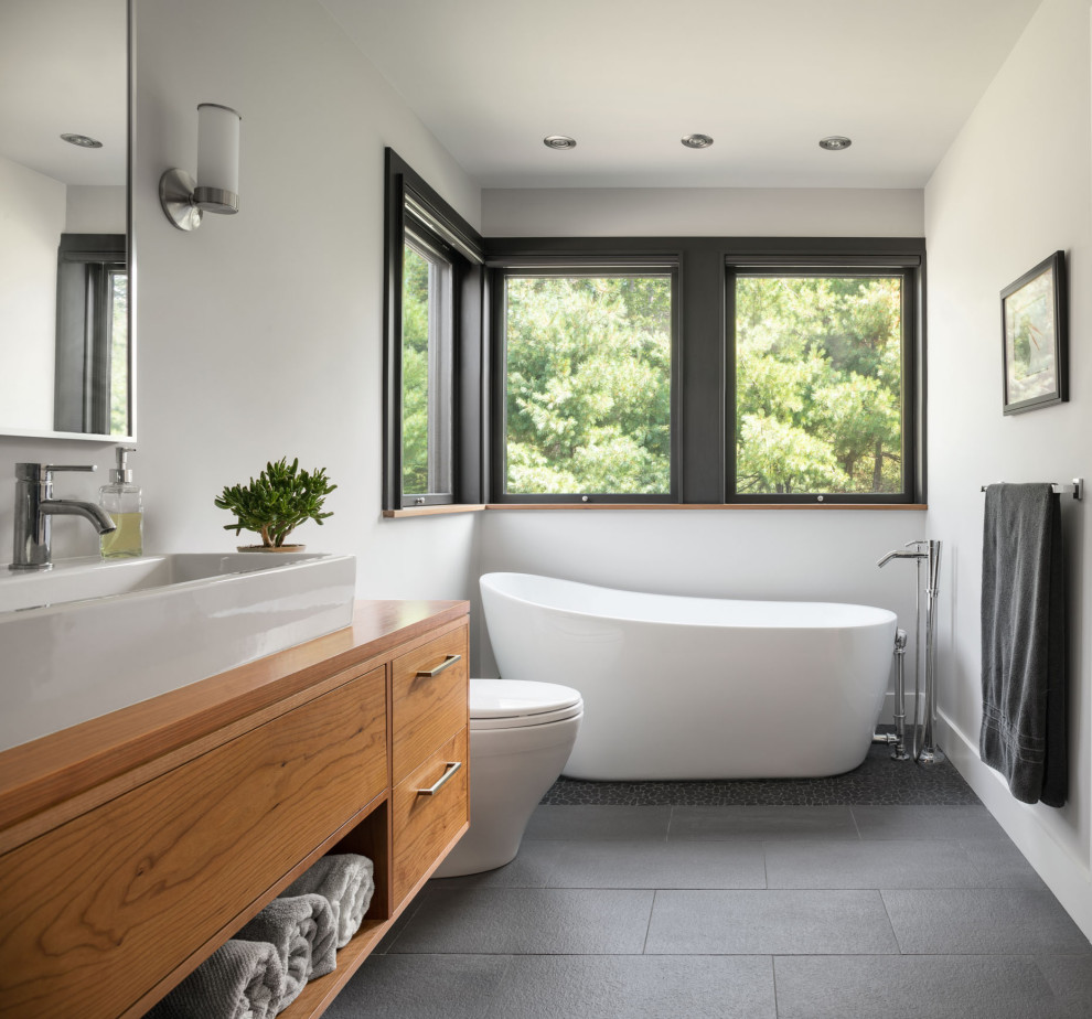 Design ideas for a large contemporary master bathroom in Other with flat-panel cabinets, medium wood cabinets, a freestanding tub, a one-piece toilet, white walls, a trough sink, wood benchtops, grey floor and beige benchtops.