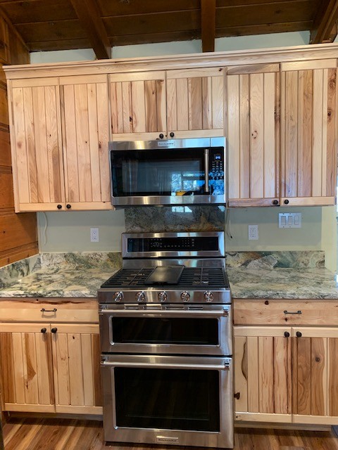Example of a mid-sized mountain style medium tone wood floor and brown floor open concept kitchen design with an undermount sink, flat-panel cabinets, light wood cabinets, granite countertops, gray backsplash, stone slab backsplash, stainless steel appliances and gray countertops