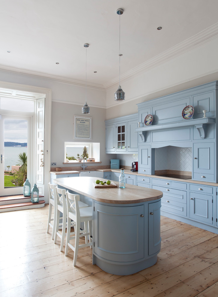 Photo of a mid-sized country l-shaped kitchen in Dublin with blue cabinets, white splashback, with island, a farmhouse sink, recessed-panel cabinets, wood benchtops, subway tile splashback, light hardwood floors and beige floor.