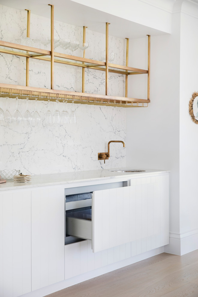 This is an example of a mid-sized beach style single-wall wet bar in Sydney with an undermount sink, white cabinets, white splashback and white benchtop.
