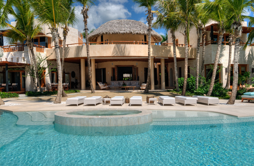 Photo of a tropical backyard round pool in Other with a hot tub and natural stone pavers.