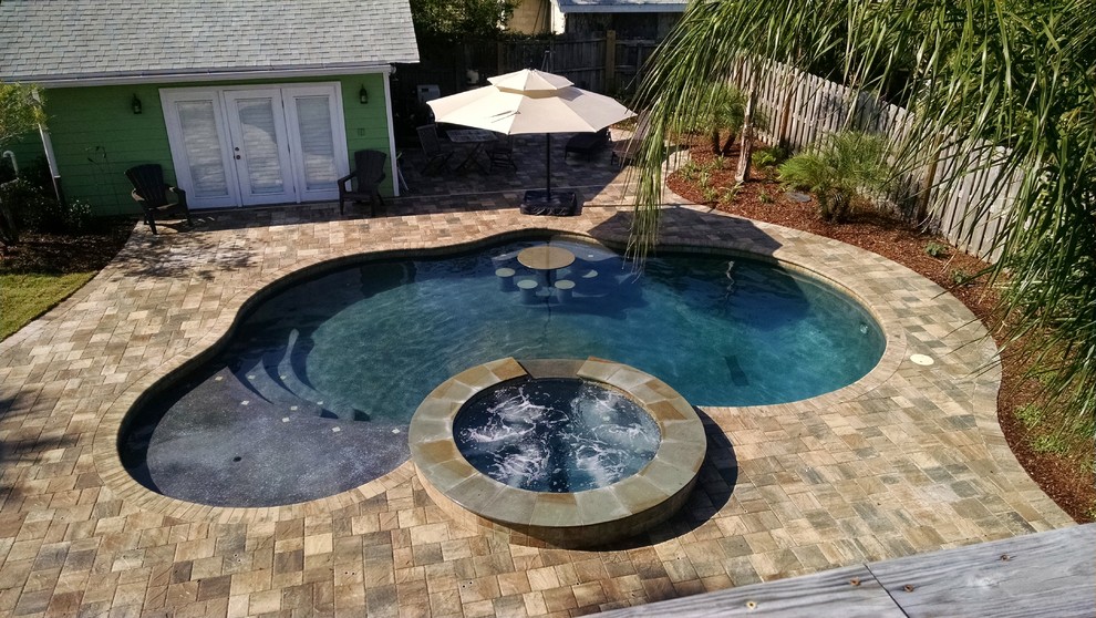 Photo of a mid-sized beach style backyard custom-shaped natural pool in Jacksonville with a hot tub and concrete pavers.