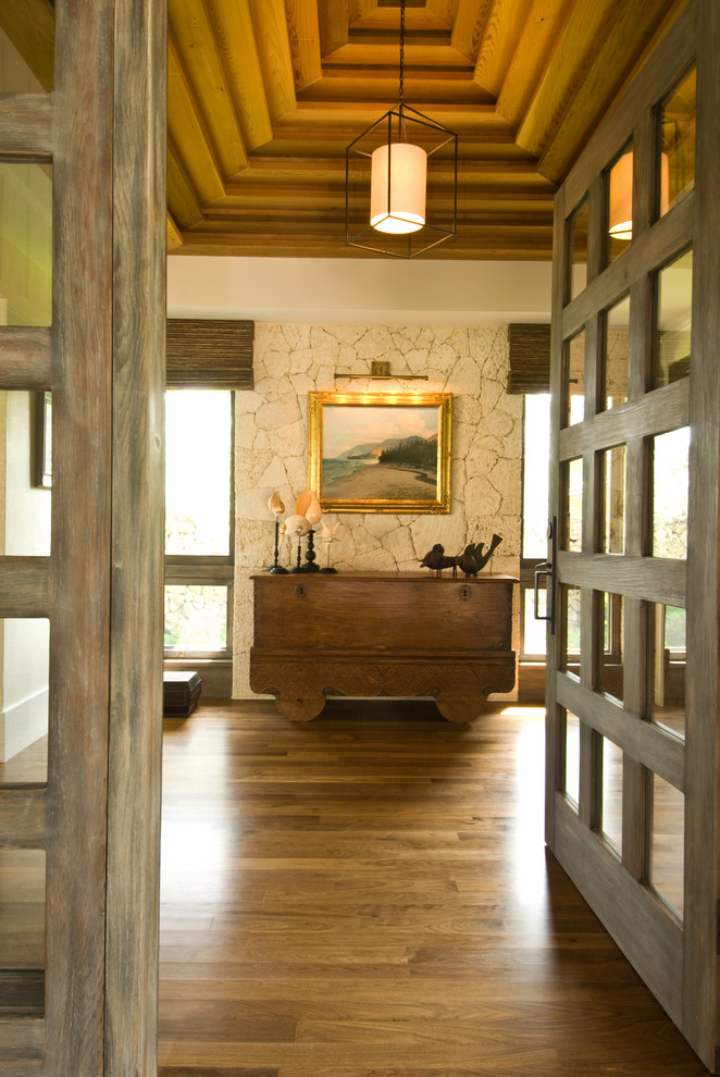 This is an example of a tropical foyer in Hawaii with dark hardwood floors and a glass front door.