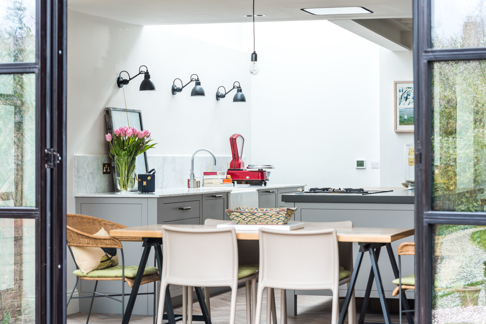 Design ideas for a large contemporary u-shaped eat-in kitchen in London with an undermount sink, flat-panel cabinets, grey cabinets, solid surface benchtops, white splashback, marble splashback, stainless steel appliances, light hardwood floors and with island.