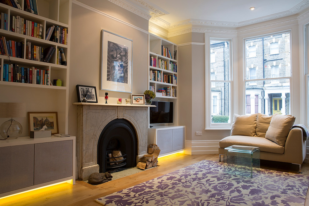 Inspiration for a large traditional enclosed living room in London with a library, brown walls, light hardwood floors, a standard fireplace, a stone fireplace surround and a freestanding tv.